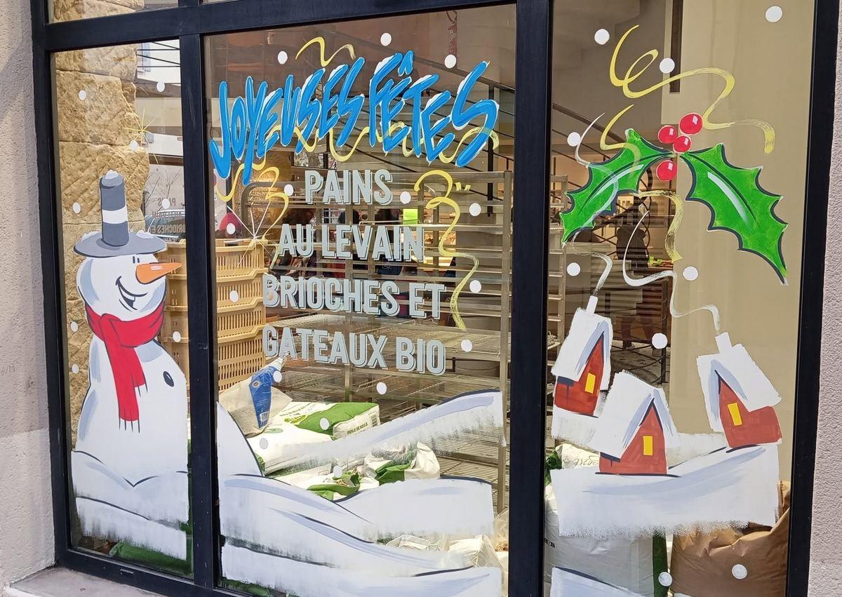 Vitrine de boulangerie bio : bonhomme de neige, houx, maisons enneigées et lettrage « Joyeuses fêtes – Pains au levain, brioches et gâteaux bio »
