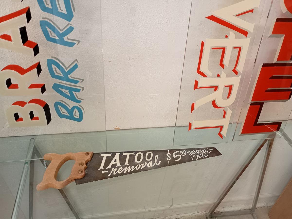 Lettrage « Tatoo removal » peint à la main sur une scie ancienne