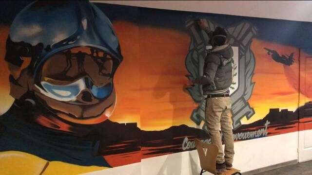 Raphaël en train de peindre le blason de la caserne, debout sur une chaise