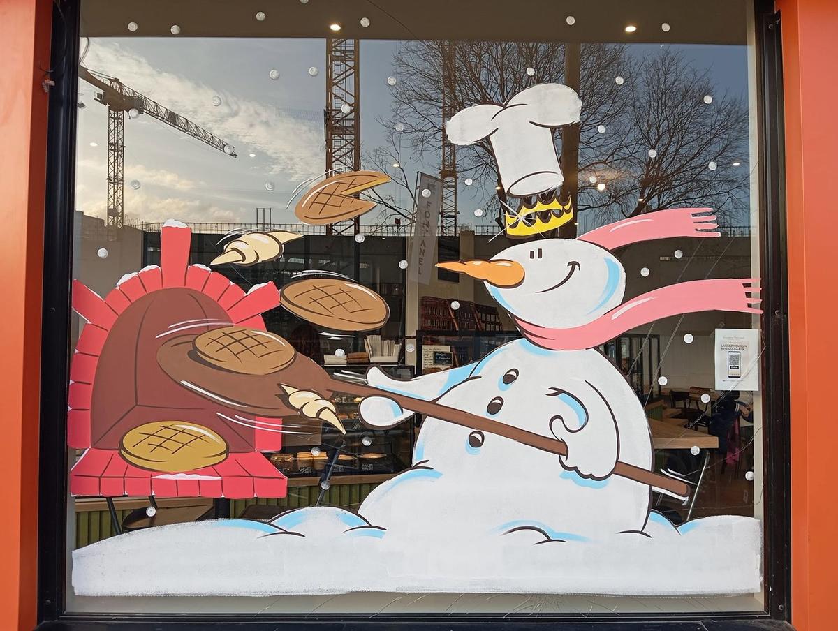 Vitrine de boulangerie peinte à la main : bonhomme de neige coiffé d'une toque et d'une couronne, enfournant galettes des rois et croissants dans un four à pain
