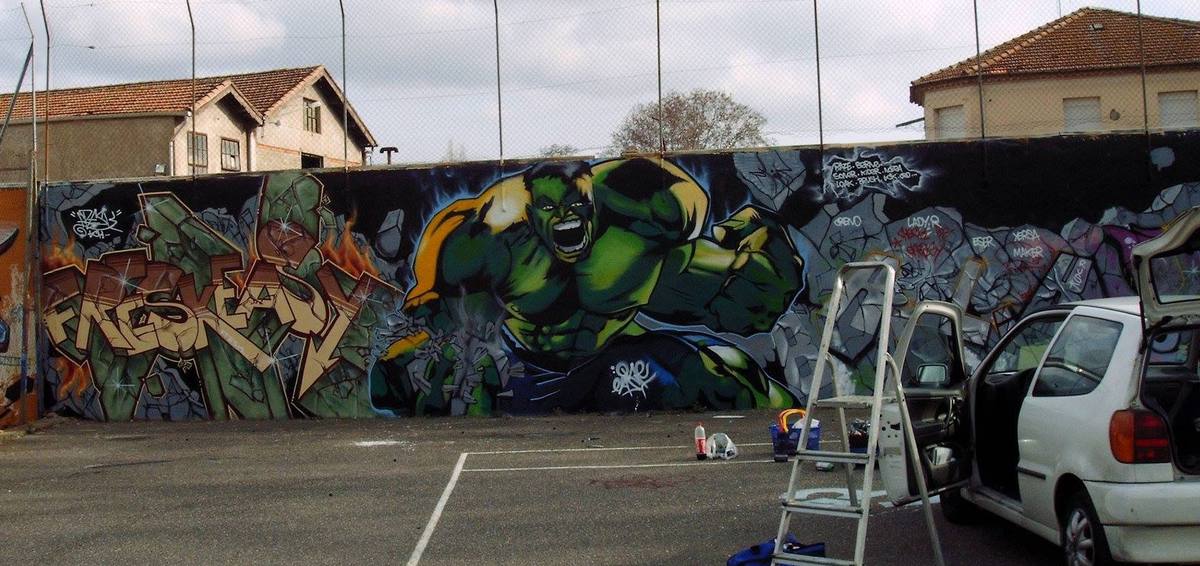 Graffiti sur le mur d'un terrain de sport : grand lettrage et personnage surgissant d'un mur de pierres