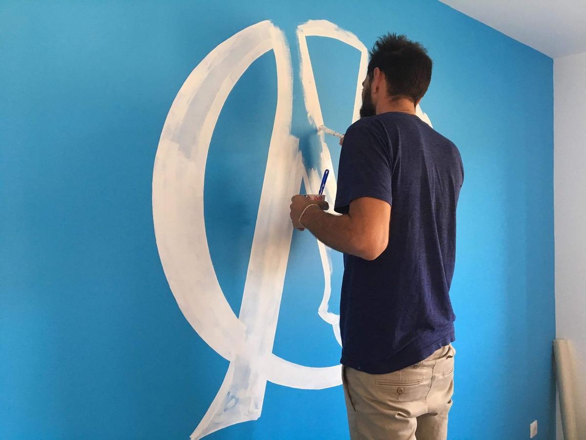 Raphaël en train de peindre le logo de l'OM en blanc sur un mur bleu