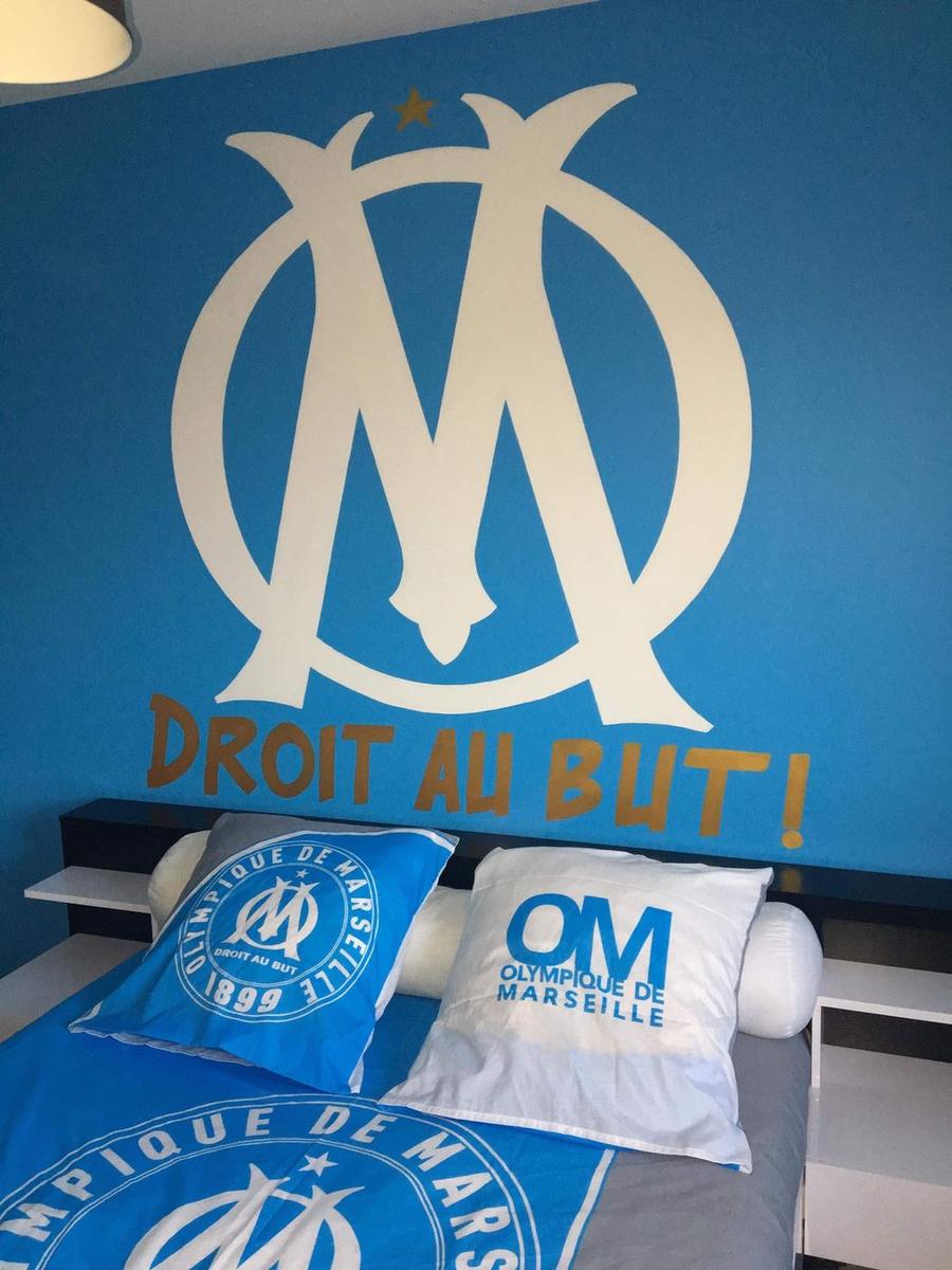 Grand logo de l'Olympique de Marseille peint au-dessus d'un lit avec l'inscription « Droit au but ! »