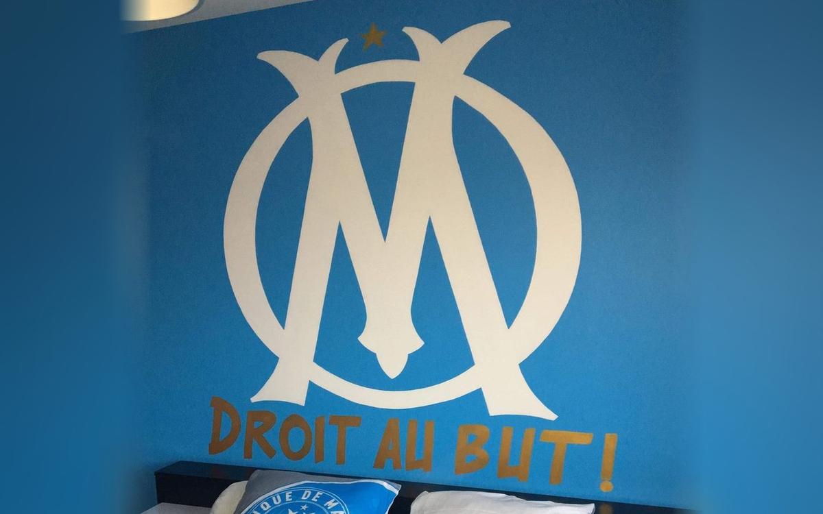 Grand logo de l'Olympique de Marseille peint au-dessus d'un lit avec l'inscription « Droit au but ! »