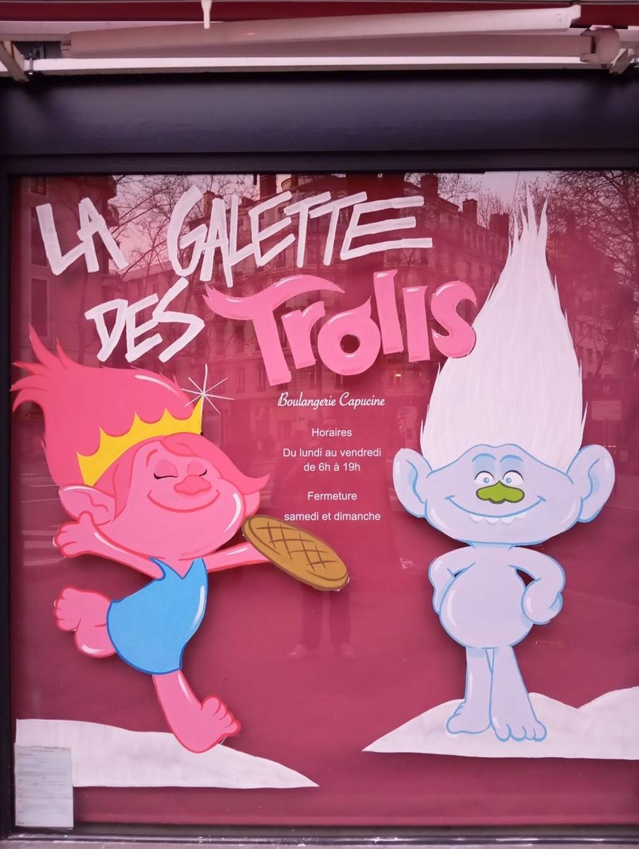 Vitrine de boulangerie « La galette des Trolls » : un troll rose couronné tenant une galette et un troll bleu, avec le lettrage peint à la main