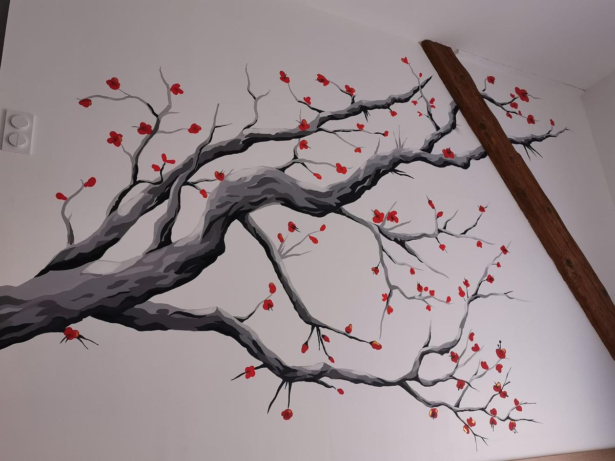 La fresque terminée : grande branche grise aux fleurs rouges peinte sur un mur blanc